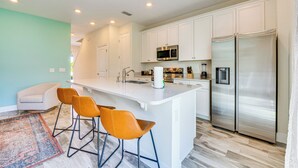Una cocina moderna con armarios blancos, electrodomésticos de acero inoxidable y una isla central con taburetes de bar.