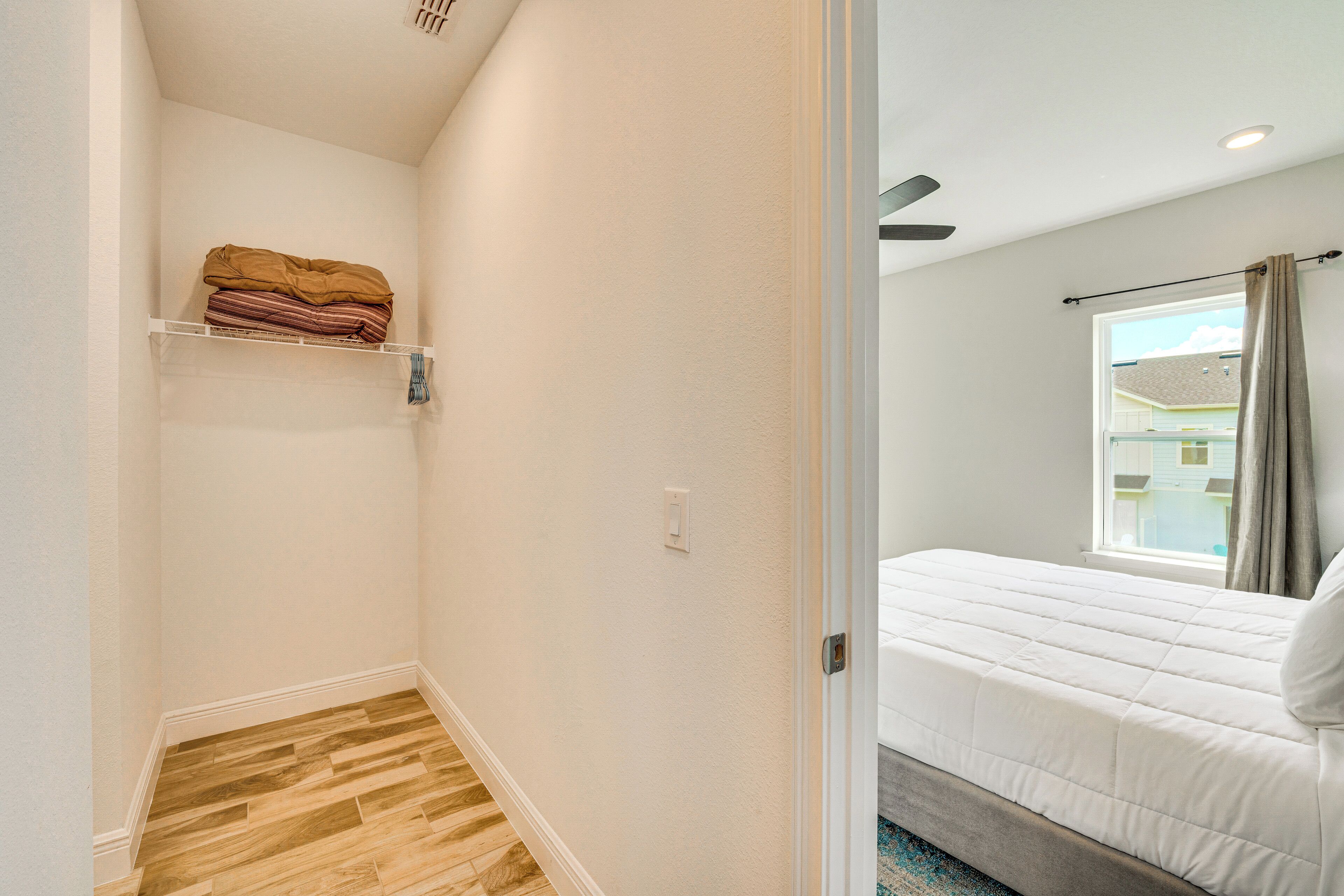 A bedroom with a bed, a window with curtains, a ceiling fan, and a small shelf with folded blankets.