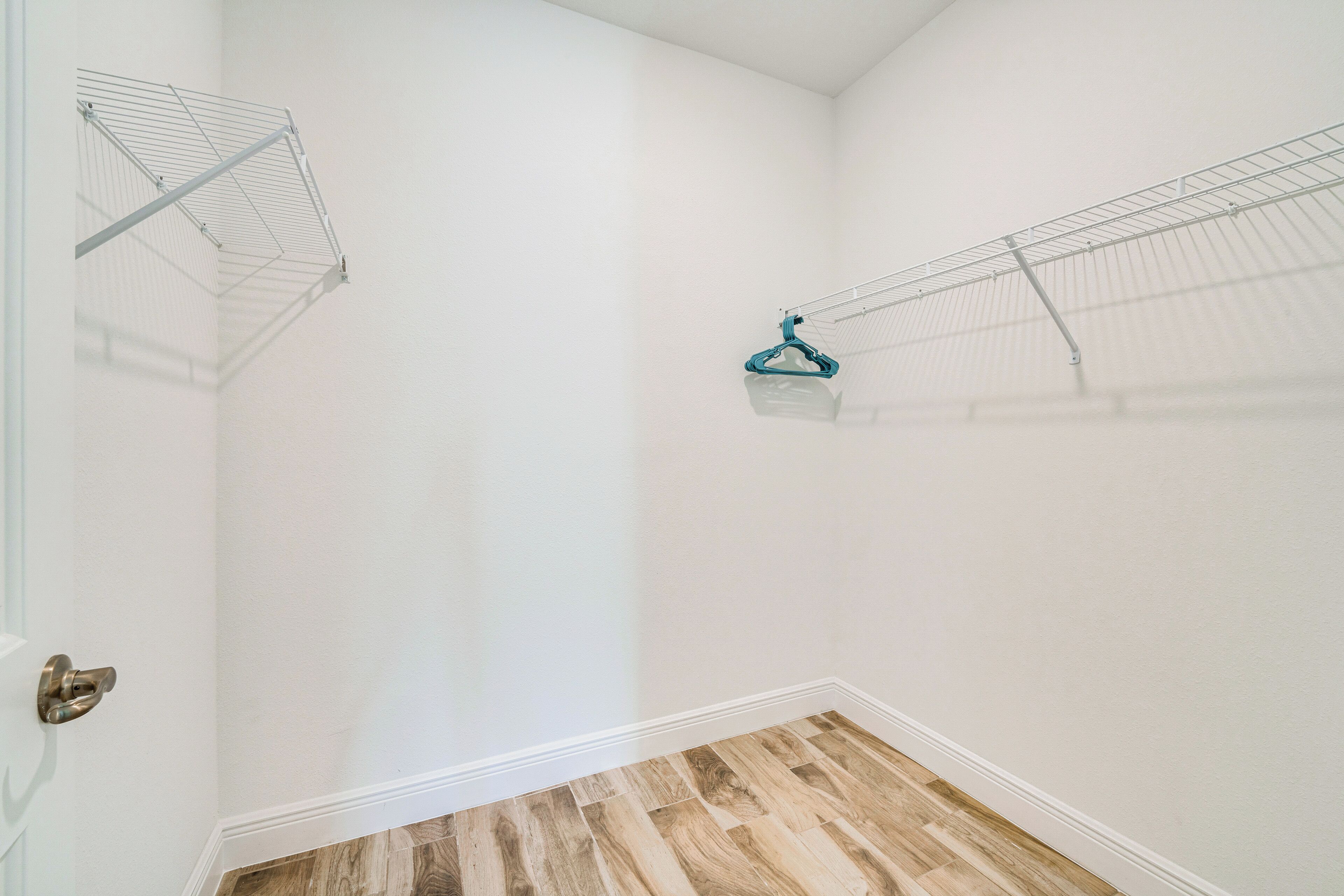 Una esquina de una habitación con suelo de madera y paredes blancas, con dos tendederos metálicos.