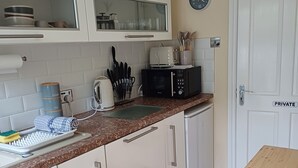 A modern kitchen with white cabinets, a microwave, a toaster, and a wooden table. - 3 Room Bedsit Flat in Nat. Reserve. Pet friendly. Free return Eden taxi B4 9pm. (Par)