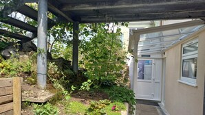A garden area with a wooden bench, a stone wall, and a variety of plants. - 3 Room Bedsit Flat in Nat. Reserve. Pet friendly. Free return Eden taxi B4 9pm. (Par)