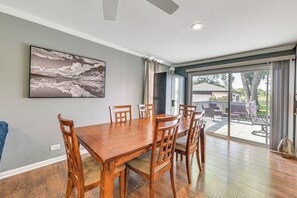A dining area with a wooden table and chairs, a large painting on the wall, and a view through a sliding glass door to an outdoor patio. - Lakefront Antioch Home w/ Dock, Grill, Game Room! (Antioch)