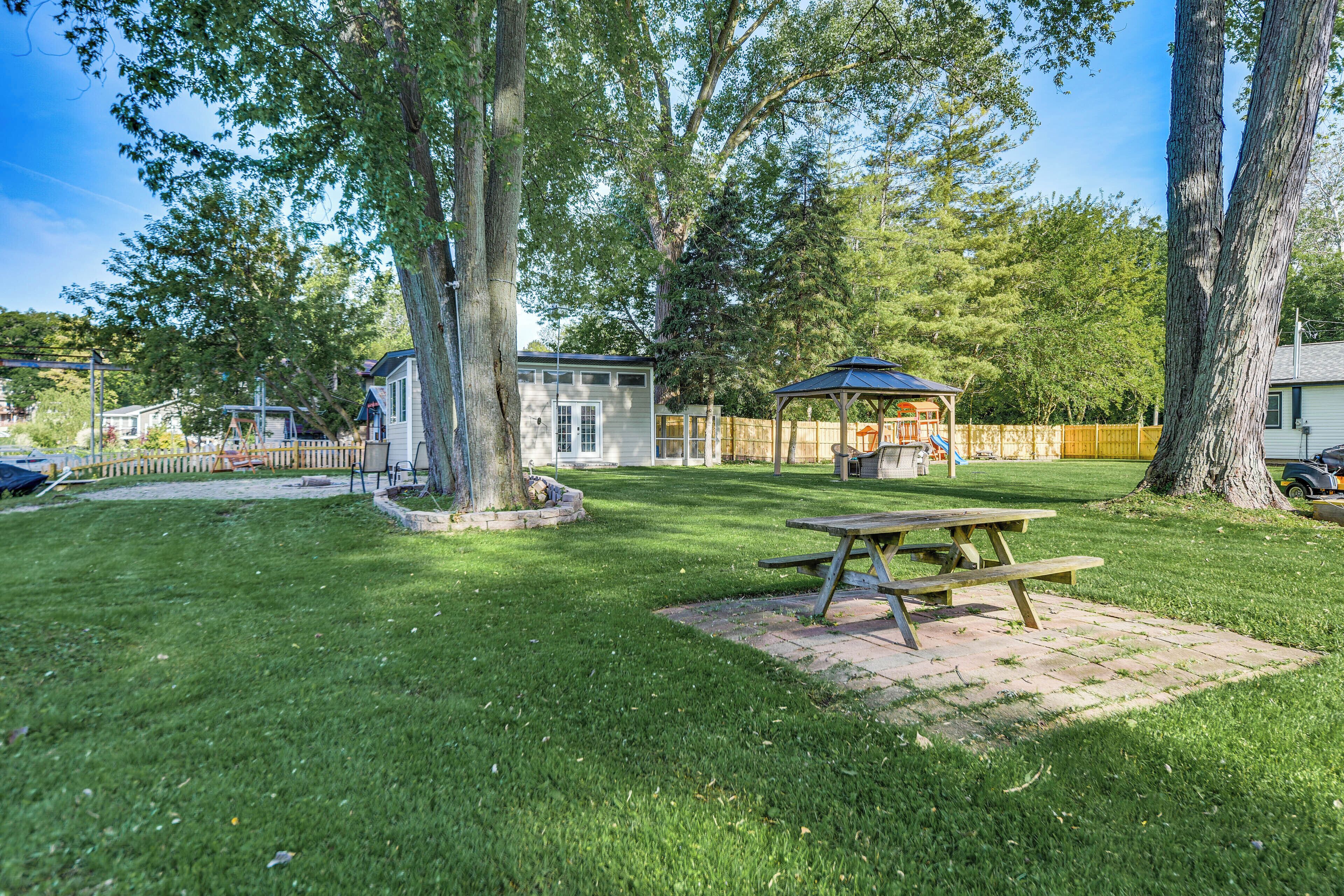 A backyard with a picnic table, a gazebo, and a fenced play area.