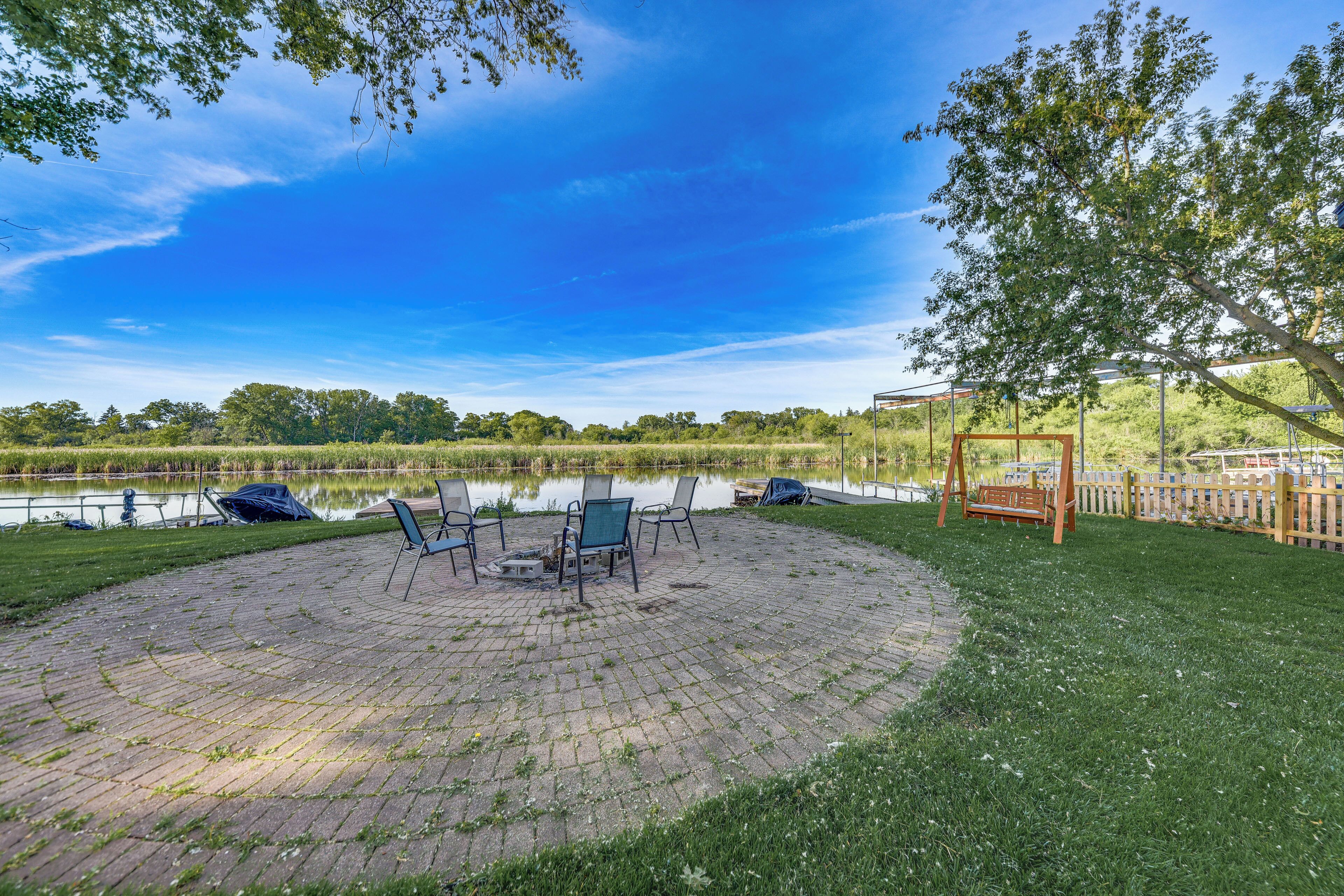 A circular brick patio with outdoor seating, a swing set, and a view of a lake.