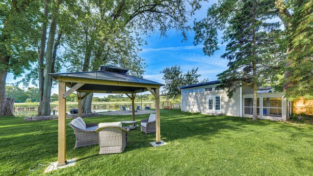 A covered outdoor seating area with wicker furniture, a small building, and a well-maintained lawn.