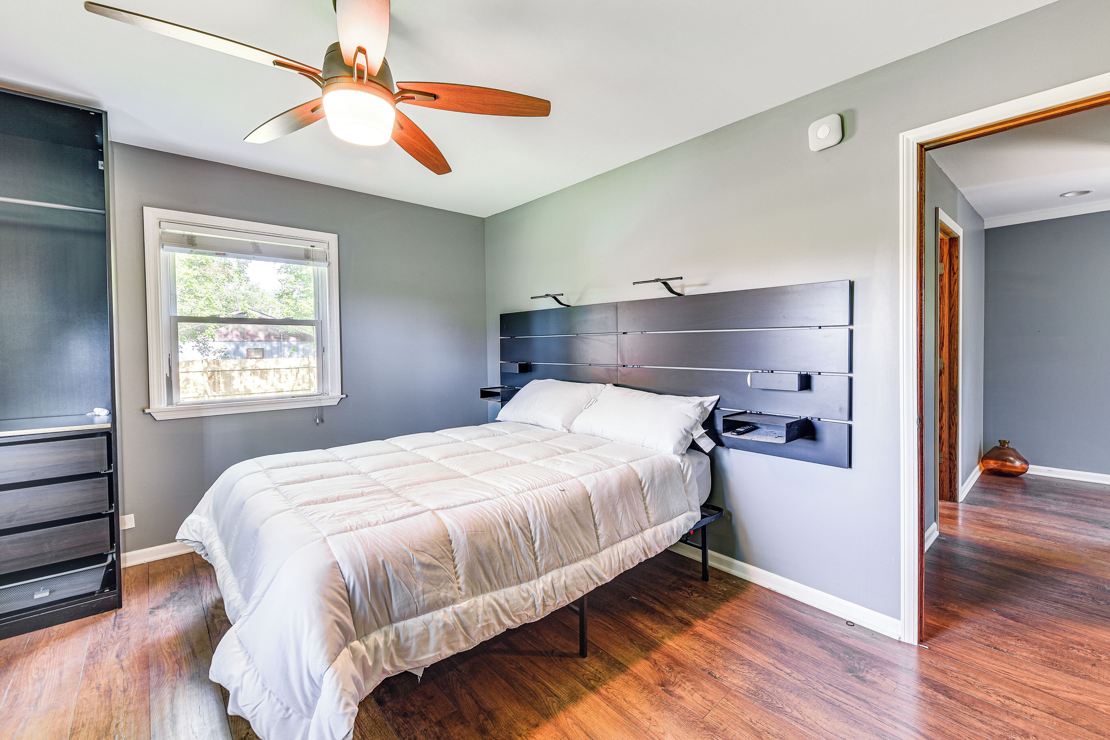 A bedroom with a bed, wooden floor, ceiling fan, and a window.