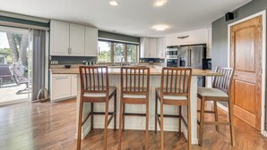 A modern kitchen with white cabinets, a central island with bar stools, and a large window providing natural light.