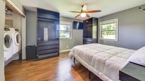 A bedroom with a bed, a ceiling fan, a window, and a built-in washer and dryer.