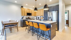 Una cocina moderna con armarios de madera, una isla central con taburetes de bar, electrodomésticos de acero inoxidable e iluminación colgante.
