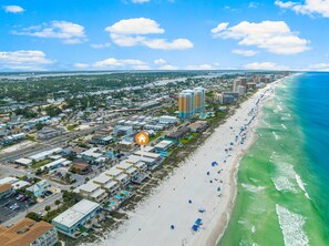 An aerial view of a coastal city with a beachfront, hotels, and a clear sky.