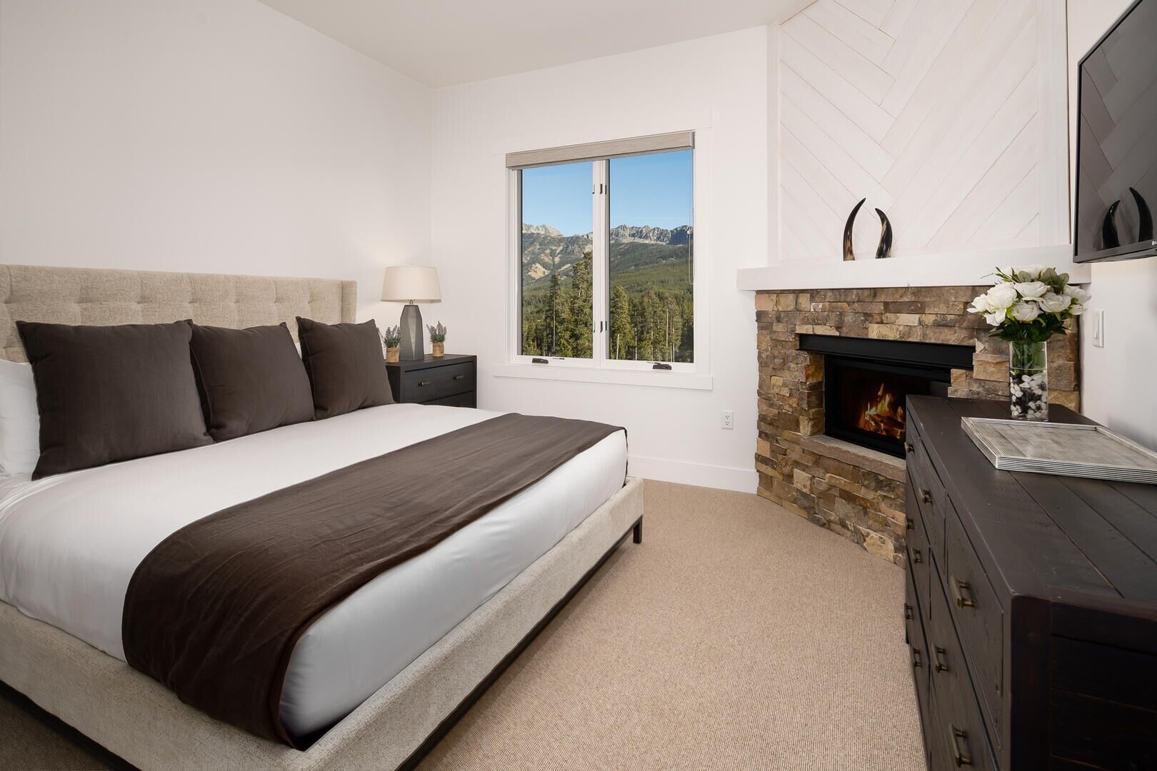 Une chambre à coucher avec un grand lit, une cheminée, une table de chevet et une fenêtre donnant sur les montagnes.