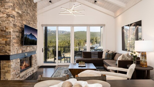 Una sala moderna con chimenea de piedra, un ventanal con vistas a la montaña, un sofá acogedor y una zona de comedor con mesa de madera.