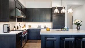 Una cocina moderna con armarios oscuros, una isla central con taburetes, una cafetera, un hervidor y un tostador.