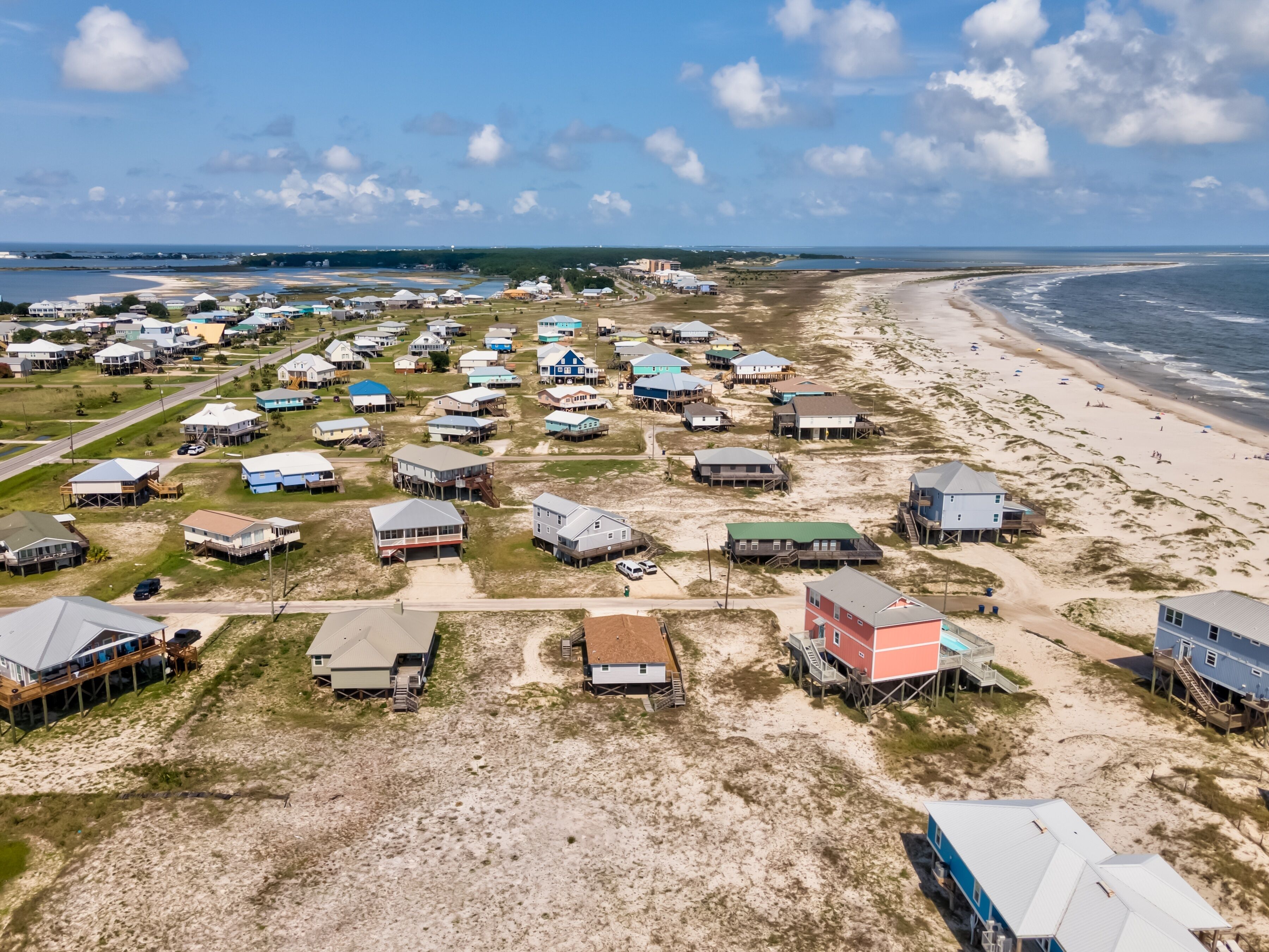 Una zona costera con numerosas casas de playa, algunas elevadas sobre pilotes, y una playa al fondo.