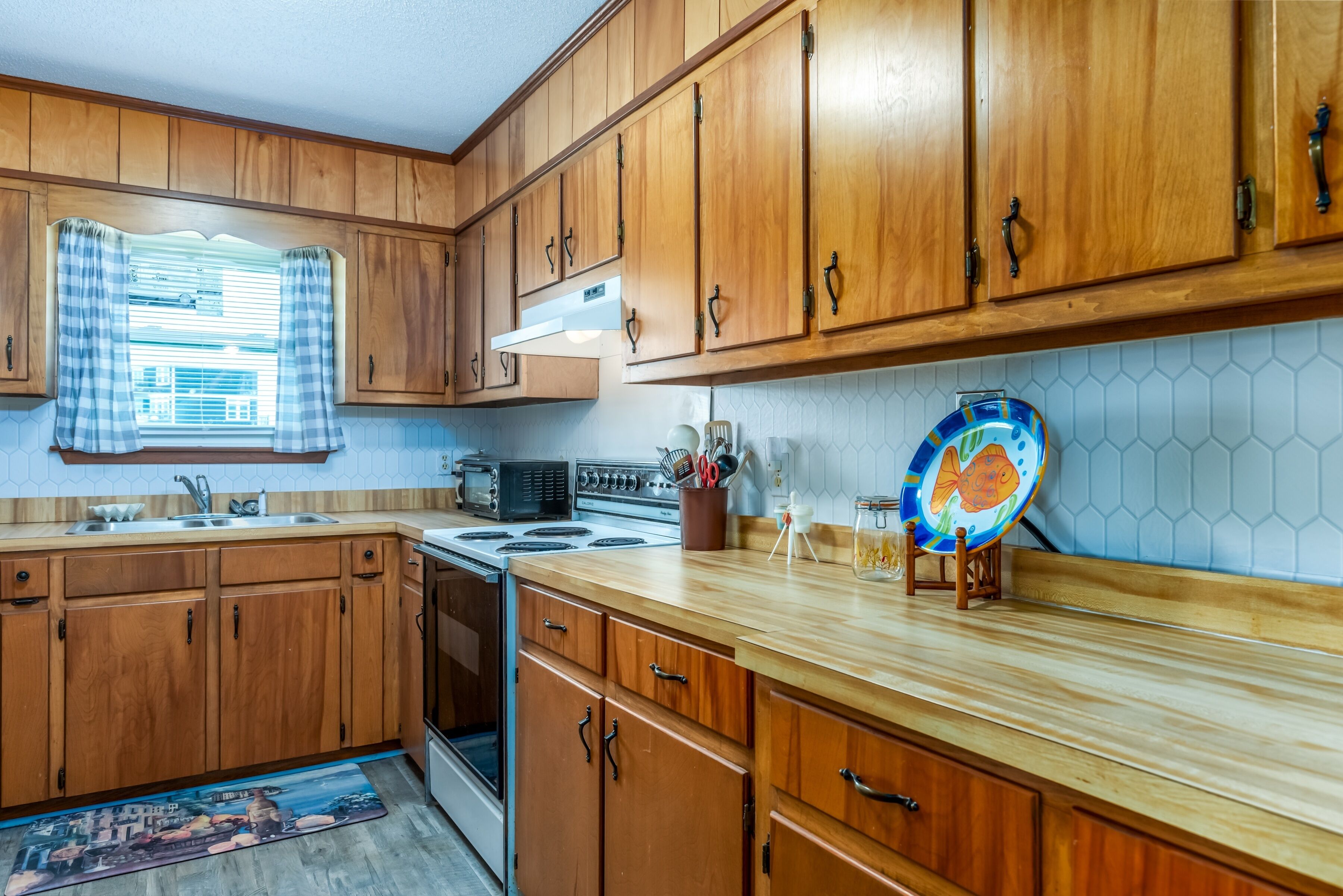 Una cocina con armarios de madera, microondas, estufa y una ventana con cortinas.