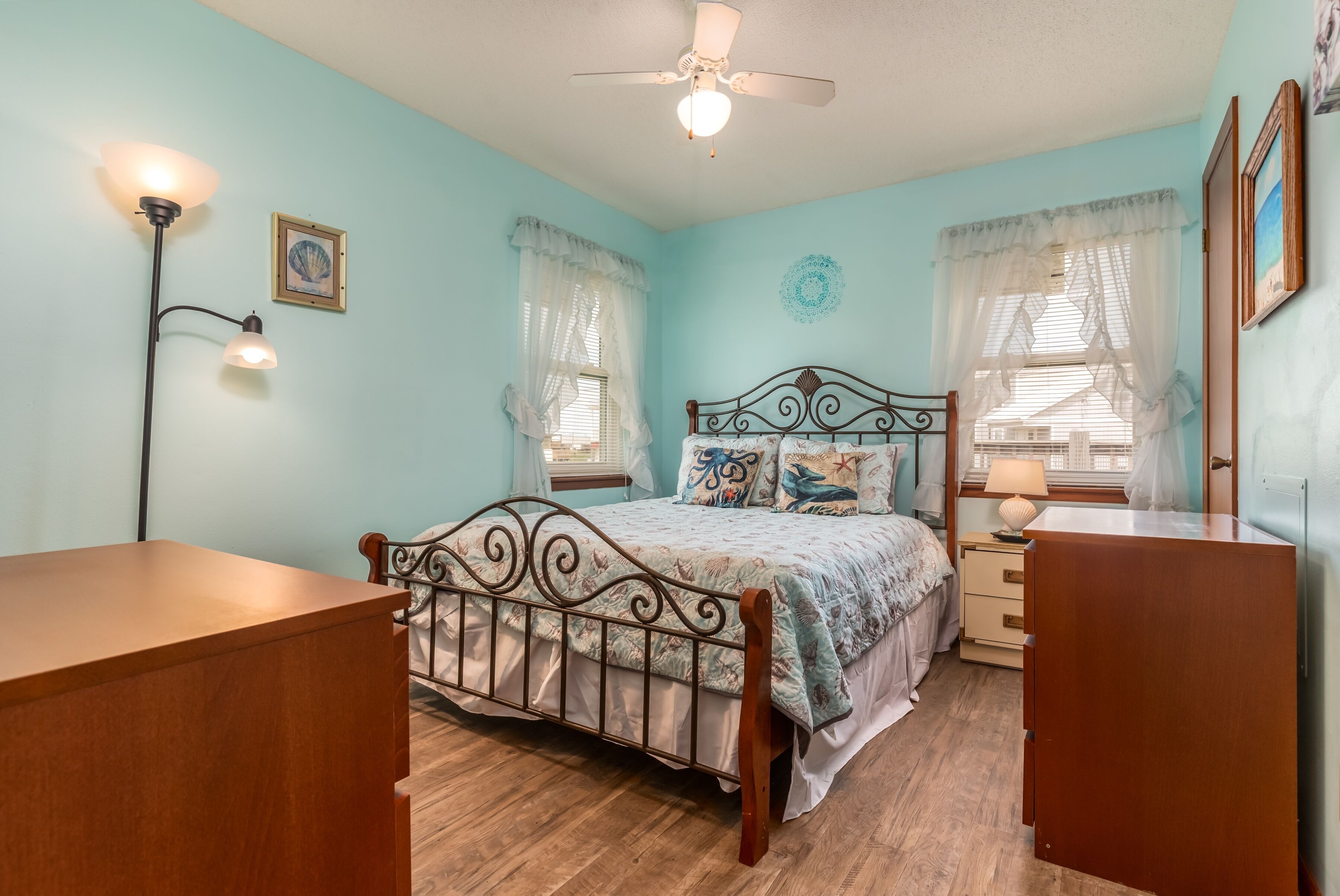 Une chambre à coucher comprenant un lit, une table de chevet, une commode, un ventilateur de plafond et deux lampes fixées au mur.