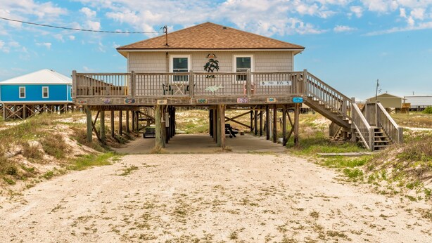 Ett hus vid stranden med en träveranda, en trappa och utsikt över stranden.