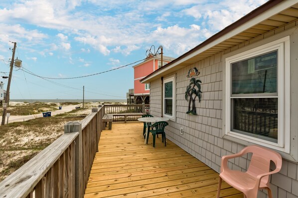 A wooden deck with a table and chairs, a pink chair, and a window with blinds.
