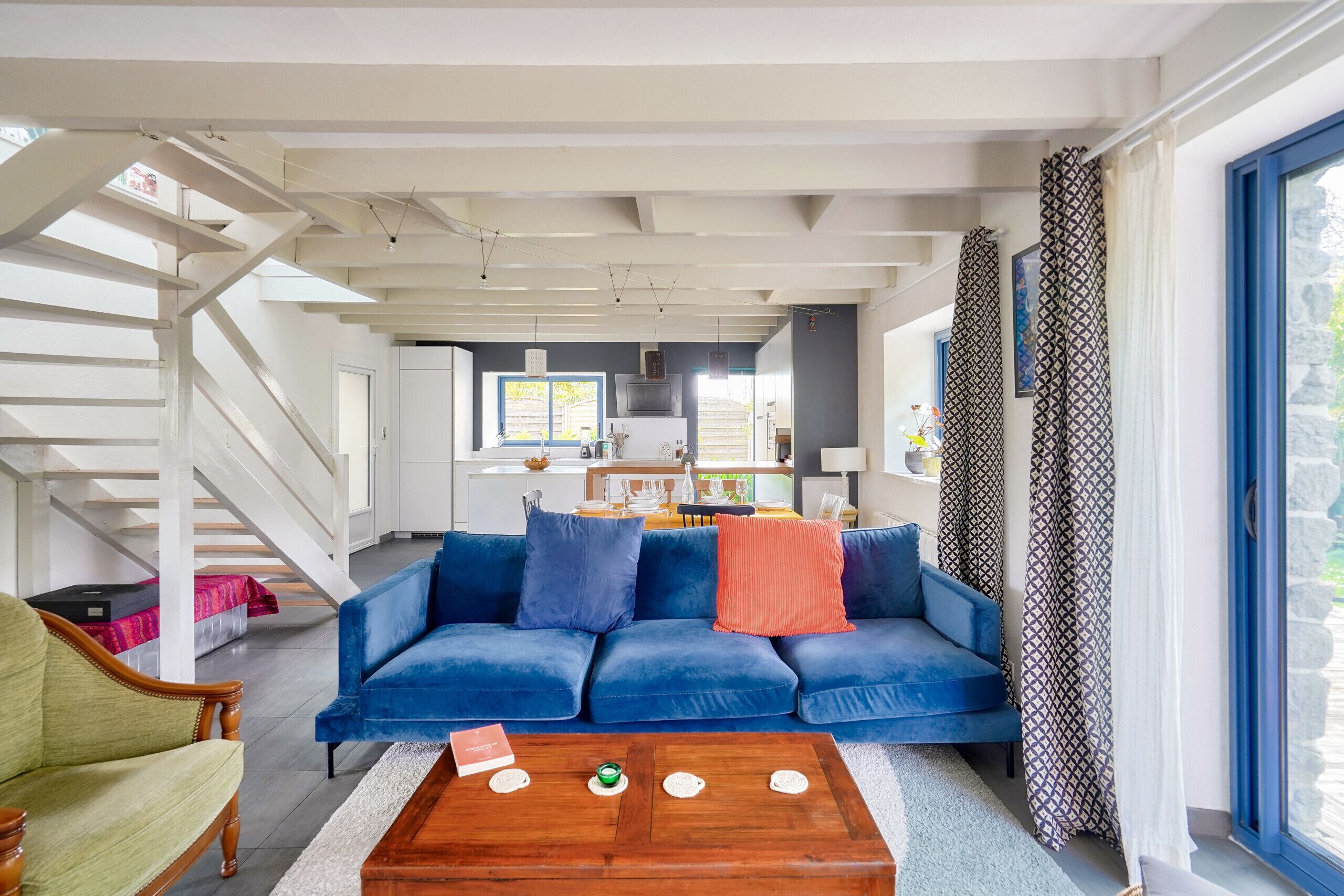 A modern living room with a blue sofa, a wooden coffee table, and a staircase leading to an upper floor.