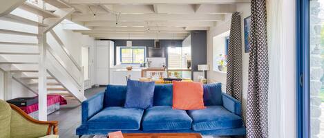 A modern living room with a blue sofa, a wooden coffee table, and a staircase leading to an upper floor.