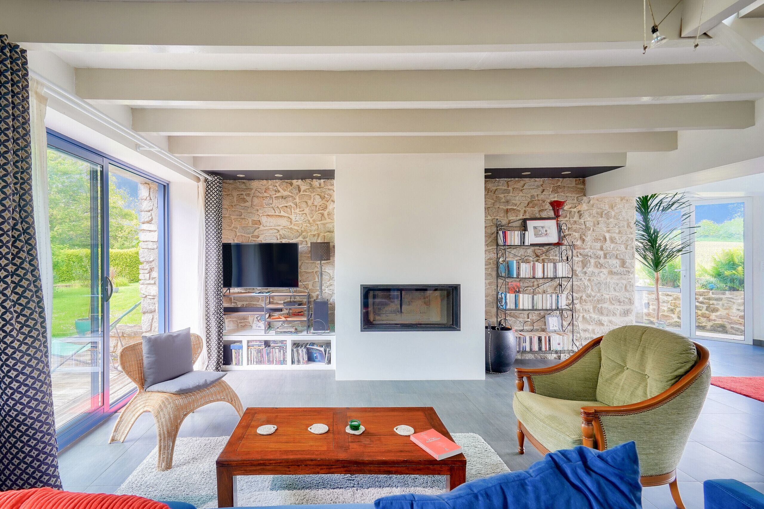 A modern living room with a stone wall, a fireplace, a television, and a bookshelf.