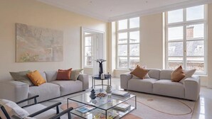 A spacious living room with two sofas, a coffee table, and large windows offering a view of buildings. - PONT NEUF - A TESTAMENT TO PARISIAN SOPHISTICATION OF 200 M2 – 3 BEDOROOM (Paris)