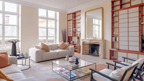 A spacious living room with a fireplace, a sofa set, a coffee table with magazines, and a large mirror. - PONT NEUF - A TESTAMENT TO PARISIAN SOPHISTICATION OF 200 M2 – 3 BEDOROOM (Paris)
