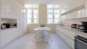 A modern kitchen with white cabinetry, a central island, and a dining table. - PONT NEUF - A TESTAMENT TO PARISIAN SOPHISTICATION OF 200 M2 – 3 BEDOROOM (Paris)