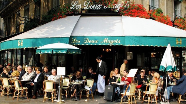 An outdoor cafe with tables and chairs, a waiter, and a sign reading "Les Deux Magots". - PONT NEUF - A TESTAMENT TO PARISIAN SOPHISTICATION OF 200 M2 – 3 BEDOROOM (Paris)