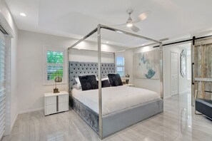 A modern bedroom with a four-poster bed, a ceiling fan, and a nightstand with a lamp. - Privacy, Heated Pool, Gulf Access and Luxury! (Bonita Springs)