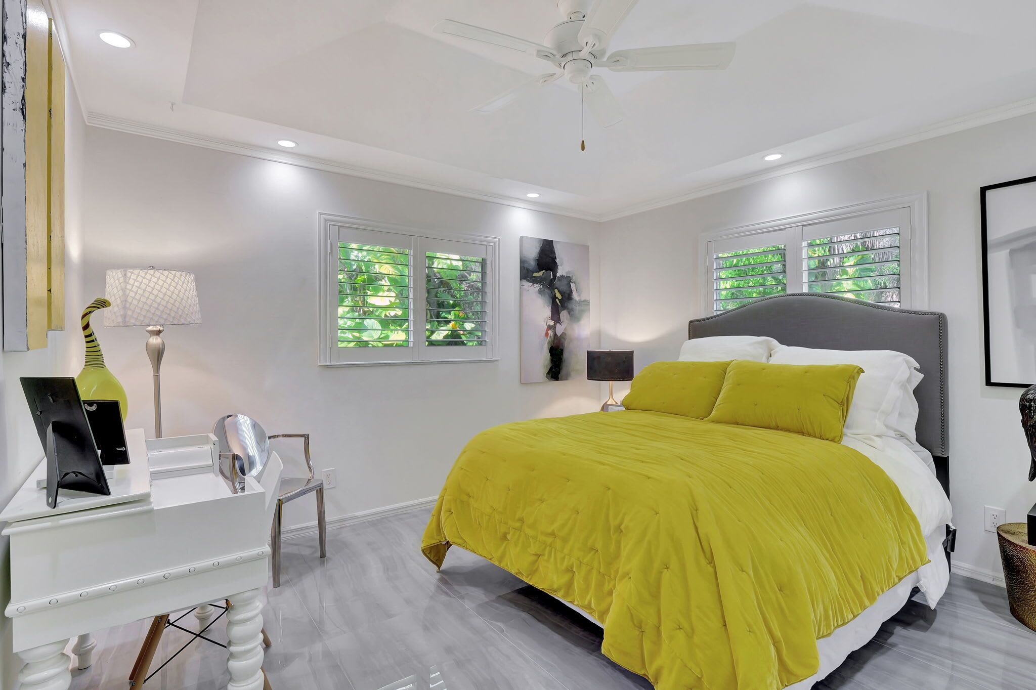 A modern bedroom with a bed, a desk, a chair, and a ceiling fan.