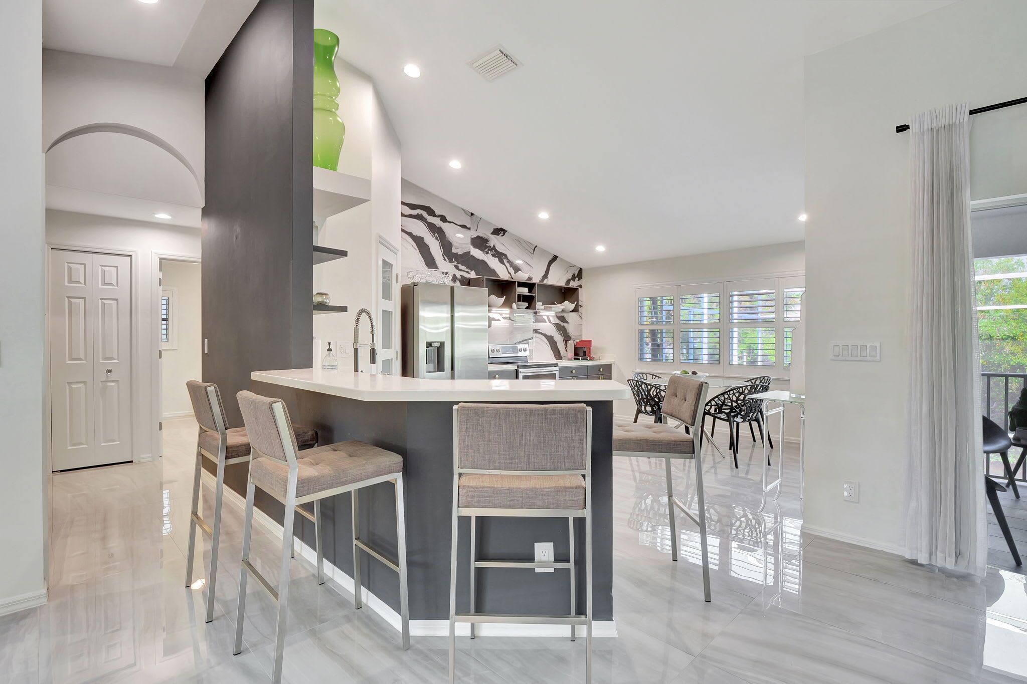 A modern kitchen with a central island, bar stools, and a dining area with chairs.