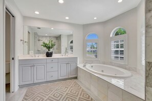 A modern bathroom with a large mirror, a bathtub, and a vanity with cabinets. - Privacy, Heated Pool, Gulf Access and Luxury! (Bonita Springs)
