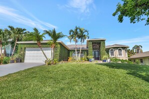 A residential property with a well-maintained lawn, palm trees, and a garage. - Privacy, Heated Pool, Gulf Access and Luxury! (Bonita Springs)