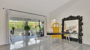 A modern interior with a glass door leading to a balcony, a yellow chair, and a large ornate mirror. - Privacy, Heated Pool, Gulf Access and Luxury! (Bonita Springs)