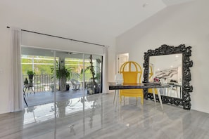 A modern interior with a glass door leading to a balcony, a yellow chair, and a large ornate mirror. - Privacy, Heated Pool, Gulf Access and Luxury! (Bonita Springs)