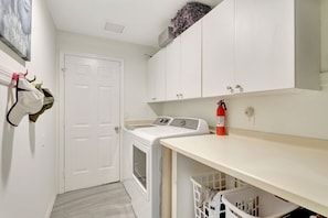 A laundry room with a washing machine, a dryer, a fire extinguisher, and a door. - Privacy, Heated Pool, Gulf Access and Luxury! (Bonita Springs)