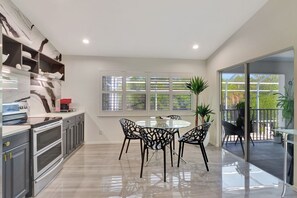 A modern kitchen with a dining area, large windows, and a view to the outside. - Privacy, Heated Pool, Gulf Access and Luxury! (Bonita Springs)