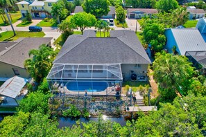 A residential house with a large glass-enclosed swimming pool, surrounded by lush greenery and palm trees. - Privacy, Heated Pool, Gulf Access and Luxury! (Bonita Springs)