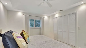 A bedroom with a bed, pillows, a window with curtains, a ceiling fan, and a closet with louvered doors. - Privacy, Heated Pool, Gulf Access and Luxury! (Bonita Springs)