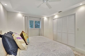 A bedroom with a bed, pillows, a window with curtains, a ceiling fan, and a closet with louvered doors. - Privacy, Heated Pool, Gulf Access and Luxury! (Bonita Springs)