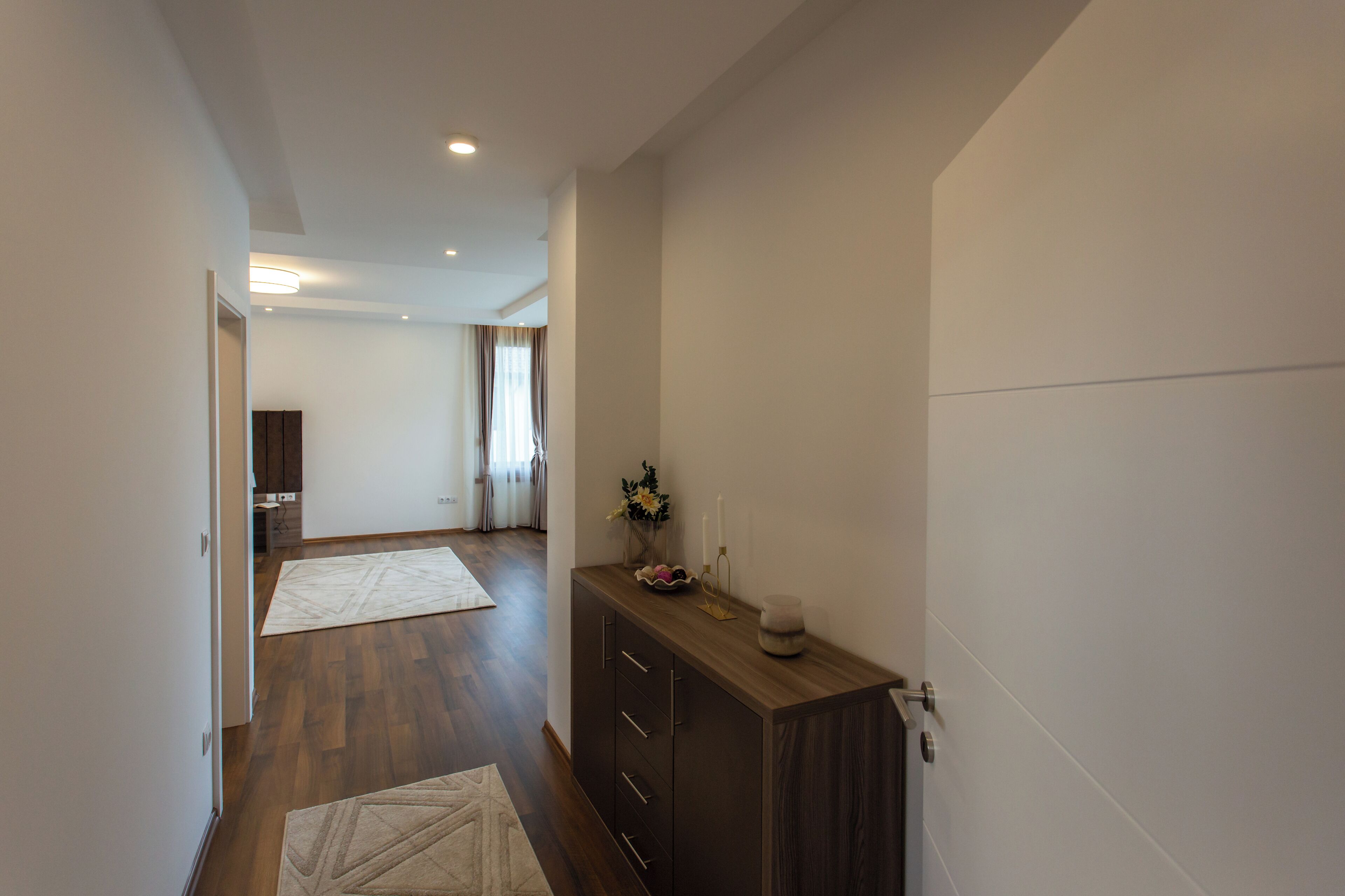 A hallway with wooden flooring, a dark wooden cabinet with drawers, and a white wall.