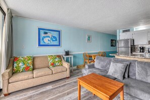 A living room with a sofa, a coffee table, a dining table with chairs, and a kitchen area with cabinets and appliances. - Royal Garden Unit 609 -  2 Bedroom, 2 Bath Oceanfront Condo (Garden City Beach)