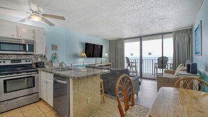 A kitchen with a microwave, oven, and dishwasher, a dining area with a table and chairs, a sofa, and a TV mounted on the wall. - Royal Garden Unit 609 -  2 Bedroom, 2 Bath Oceanfront Condo (Garden City Beach)