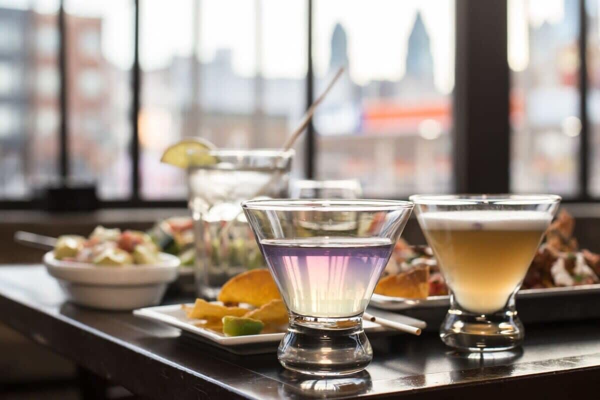 A bar area with a city view, featuring a variety of drinks and appetizers.