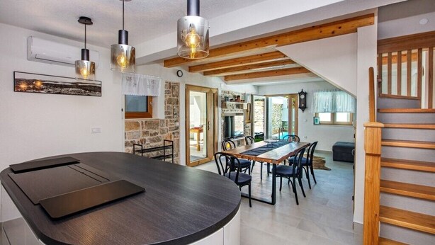 Een moderne keuken met een gebogen kookeiland, hanglampen en een eethoek met een houten tafel en stoelen.