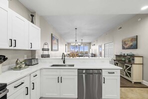 A modern kitchen with white cabinetry, a stainless steel dishwasher, and a large island with a sink.