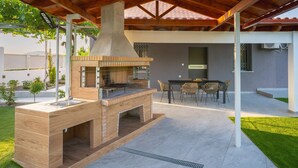 An outdoor kitchen with a grill, a sink, and a dining area with chairs and a table.