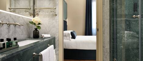 A modern bathroom with a marble sink, a glass shower enclosure, and a bed with a dark headboard.