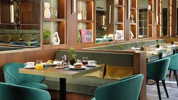 A restaurant with a long counter, green upholstered seating, and a variety of decorative items on shelves.